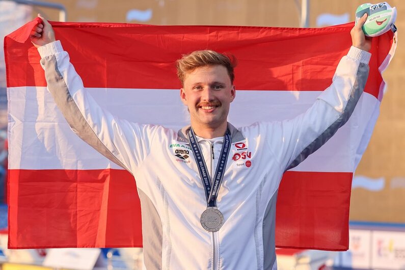 Ein Foto, das den Schwimmer Simon Bucher beim Halten der österreichischen Nationalfahne zeigt.