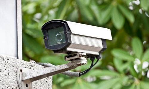 Das Bild zeigt eine Außenüberwachungskamera, die an einem weißen Gebäude montiert ist.