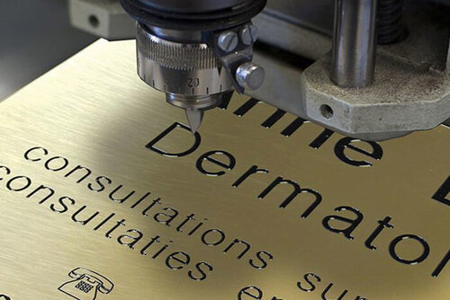 Das Bild zeigt ein Schild mit einem Text, das gerade graviert wird.